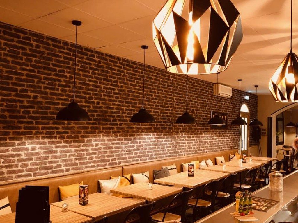Un long mur de briques et une banquette, sous de grandes suspensions dorées