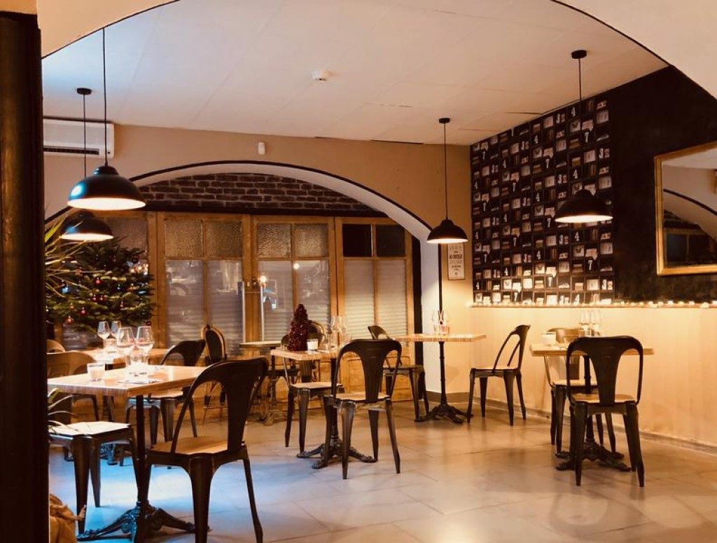 La salle du café : tables en bois, suspensions, bar au fond et grandes fenêtres cintrées
